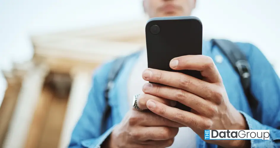 Close-up of a person holding a smartphone outdoors, with a blurred building and columns in the background.